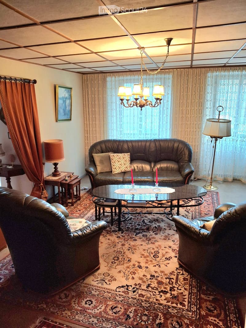 A well-furnished living room with a leather sofa, glass coffee table, armchairs, table lamps, a chandelier, side tables, and a picture frame on the wall.