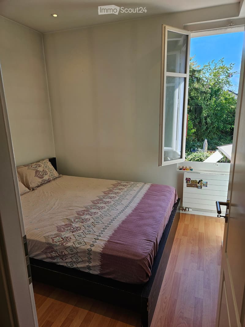 Cozy bedroom with a single bed, patterned bedding, and a small balcony with a view of greenery.