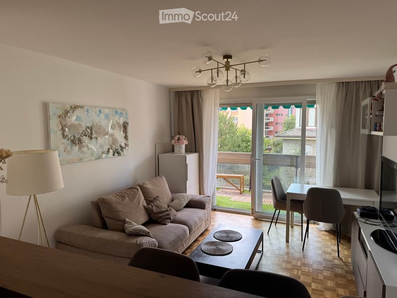 Modern living room with a beige sofa, coffee table, dining table, chairs, floor lamp, artwork, and a view to a balcony.