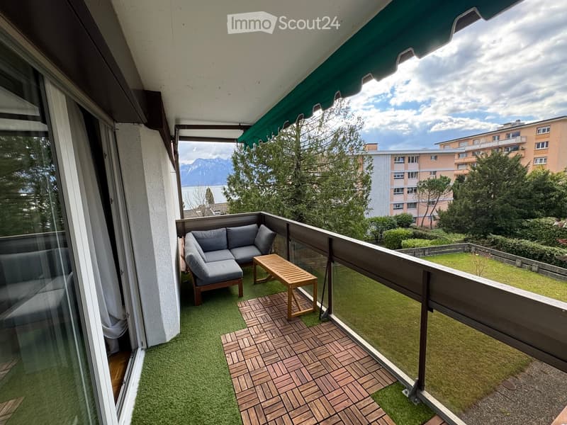 Balcony with green artificial turf, wooden decking, grey sofa, and small wooden table.