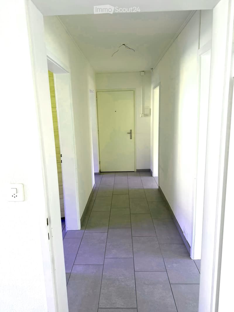 Empty hallway with tiled floor, white walls, and a closed door at the end.