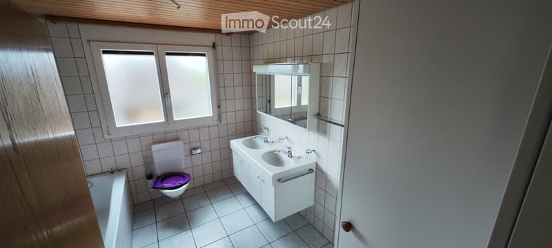 Modern bathroom with white tiles, a double sink vanity, a toilet with a purple seat cover, a bathtub, and a large mirror above the sink.