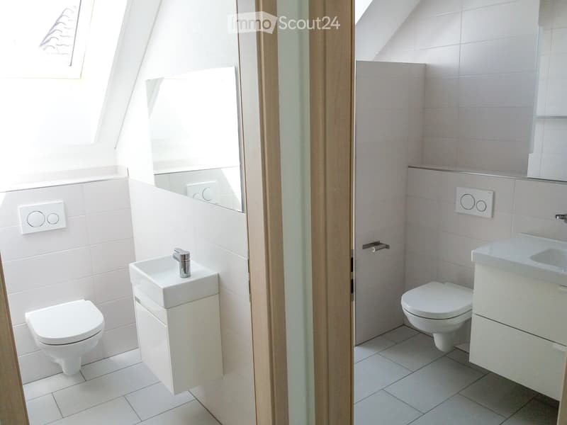 Modern, compact bathroom with white tiles, two toilets, and a sink with a chrome faucet.