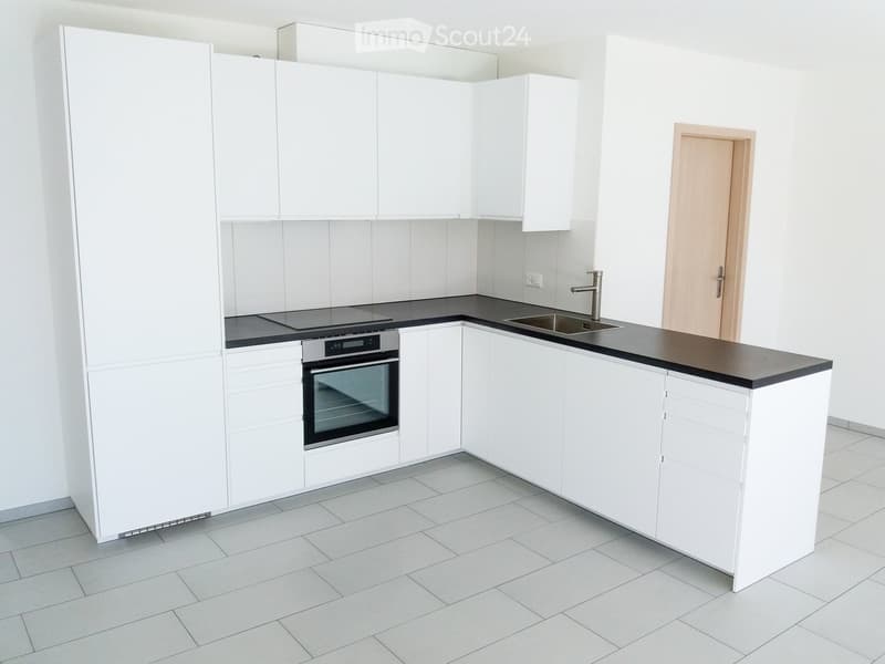 Modern kitchen with white cabinets, black countertops, and tiled flooring. Features an oven, sink, and faucet.