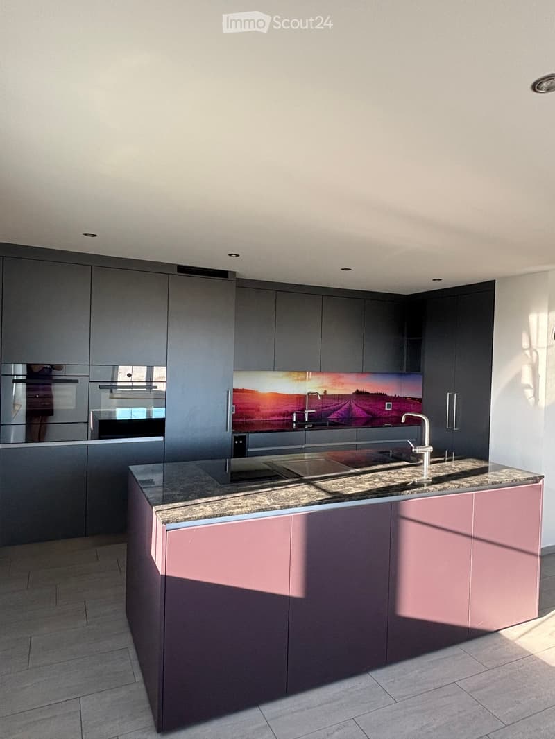 Modern kitchen with grey and pink cabinets, granite countertop, stainless steel sink, and built-in oven.