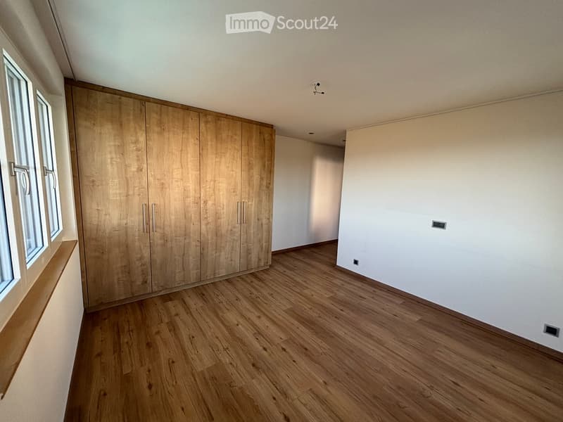 Empty room with wooden flooring, white walls, large built-in wooden wardrobe, and a window with a wooden sill.