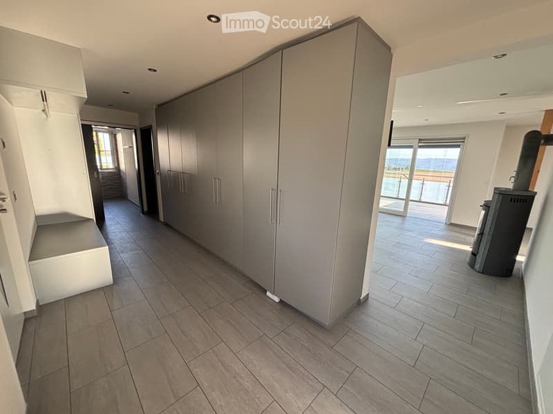 Modern hallway with grey tiled flooring, built-in storage units, and large windows leading to a balcony area.