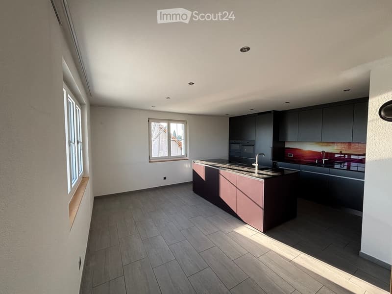 Modern kitchen with grey cabinets, a central island, and a sink, featuring tiled flooring and large windows.