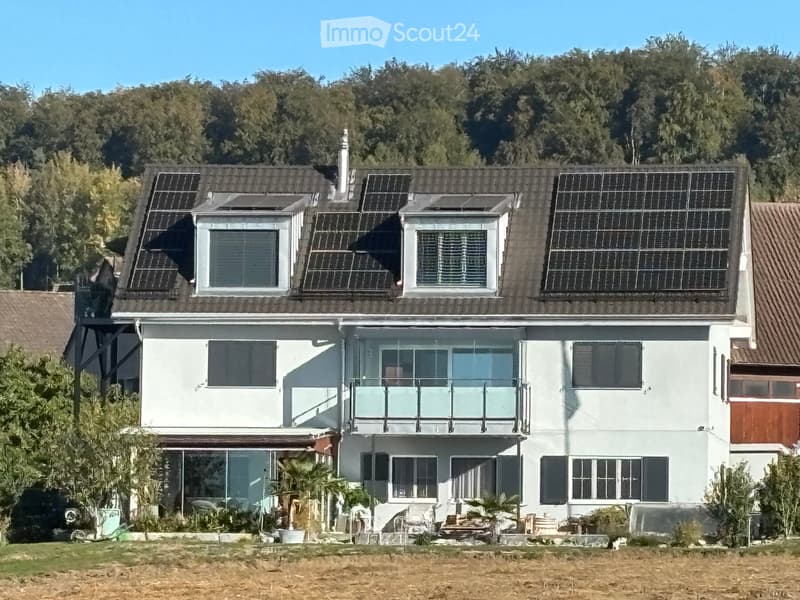 Two-story house with white exterior, solar panels on the roof, multiple windows, and a balcony on the upper level.