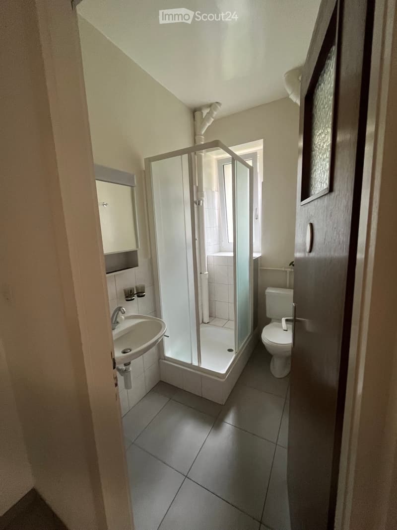 Modern bathroom with a white tiled shower, sink, and toilet. Features include a glass shower enclosure, a built-in cabinet, and a small window for natural light.