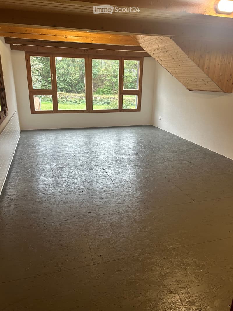 Empty room with wooden slat flooring, large windows, and exposed wooden beams on the ceiling.