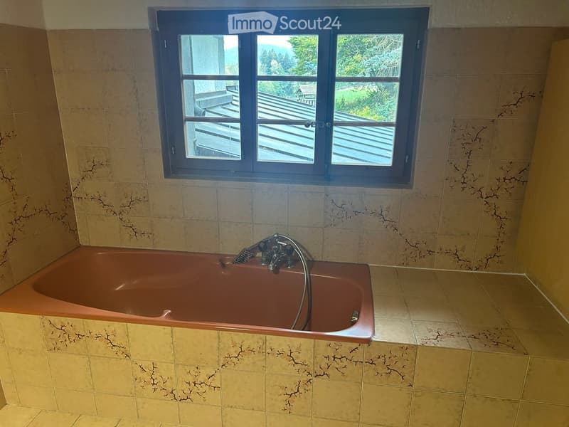 Bathroom with a brown bathtub, beige tiled walls and floor, and a window overlooking a deck and outdoor area.