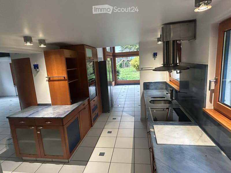 Modern kitchen with wooden cabinets, marble countertops, stainless steel sink, and a large window overlooking a garden.