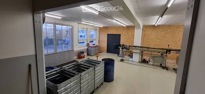 Empty industrial-style room with exposed brick wall, large windows, metal shelving units, and various storage items including barrels and crates.