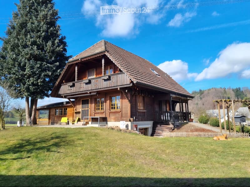 Two-story wooden house with a tiled roof, large windows, and a spacious front yard with a dog lying on the grass.