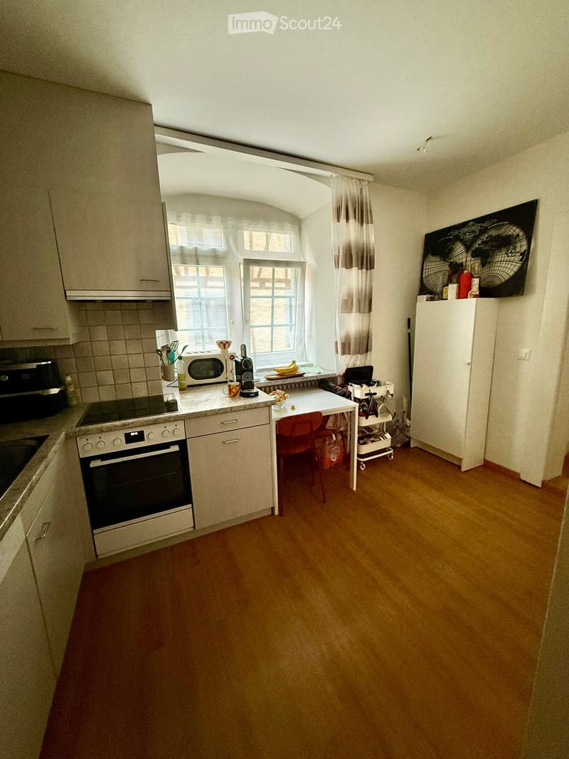 Bright kitchen with wooden flooring, white cabinets, and stainless steel appliances. Features an oven, microwave, refrigerator, and a small dining area with a table and chairs.