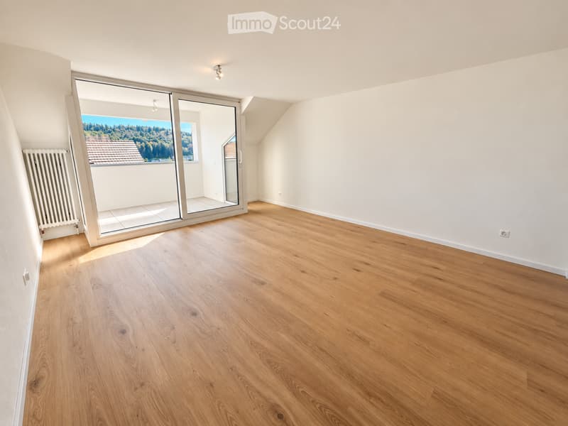Empty room with wooden flooring, large sliding glass doors leading to a balcony with scenic view, white walls, and modern lighting fixtures.