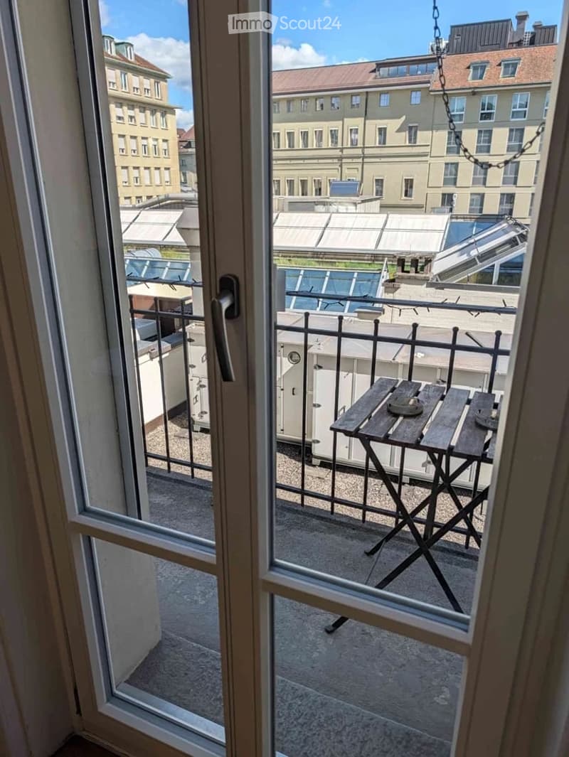 Balcony with a view of the city, featuring a single wooden chair and a small table.