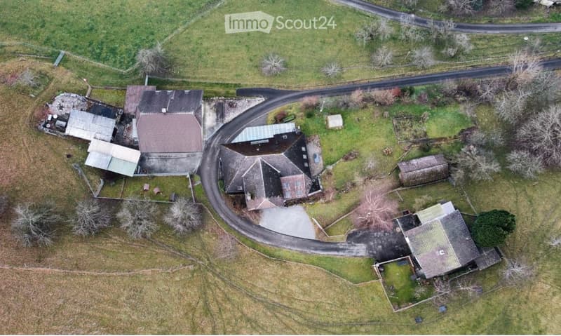 Aerial view of a rural property with multiple buildings, including a main house, outbuildings, and a driveway, surrounded by open fields and trees.