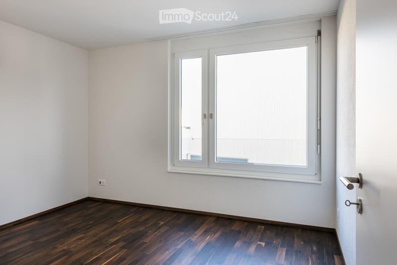 Empty room with wooden flooring, white walls, and a large window with blinds. No furniture or equipment is present.