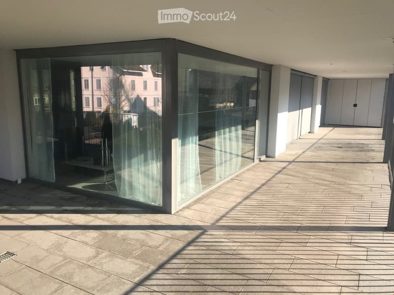 Modern balcony with large glass sliding doors, tiled floor, and a view of neighboring buildings.