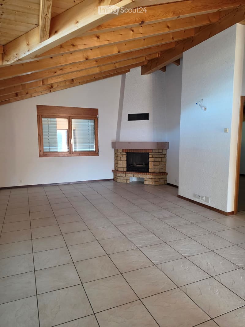 Empty room with exposed wooden beams, tiled floor, fireplace, and a window with blinds.