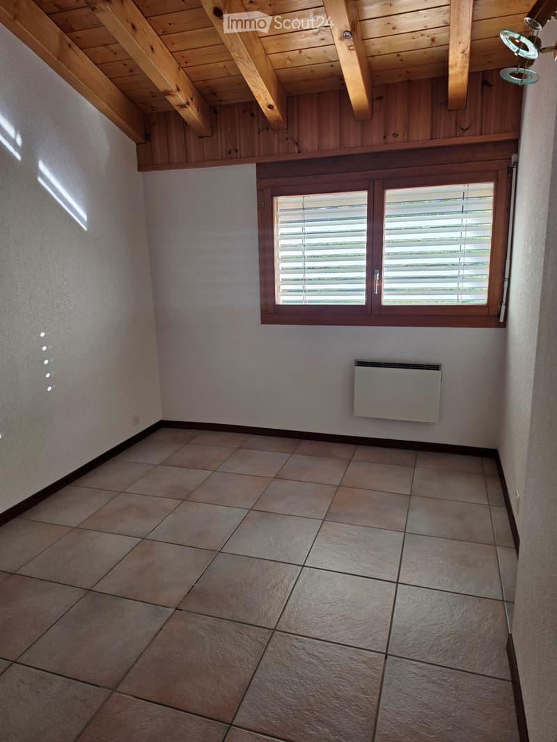 Empty room with tiled floor, wooden ceiling beams, and a window with blinds. No furniture or equipment present.