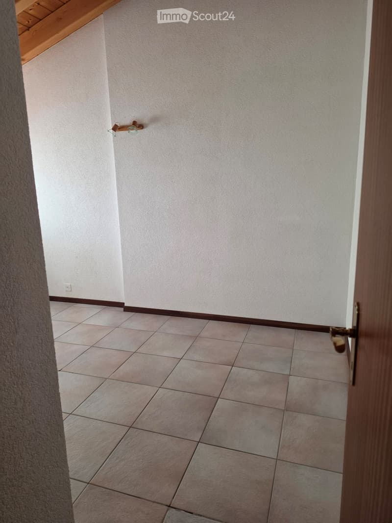 Empty room with tiled floor and light-colored walls, featuring a wooden door frame and a small light fixture on the wall.