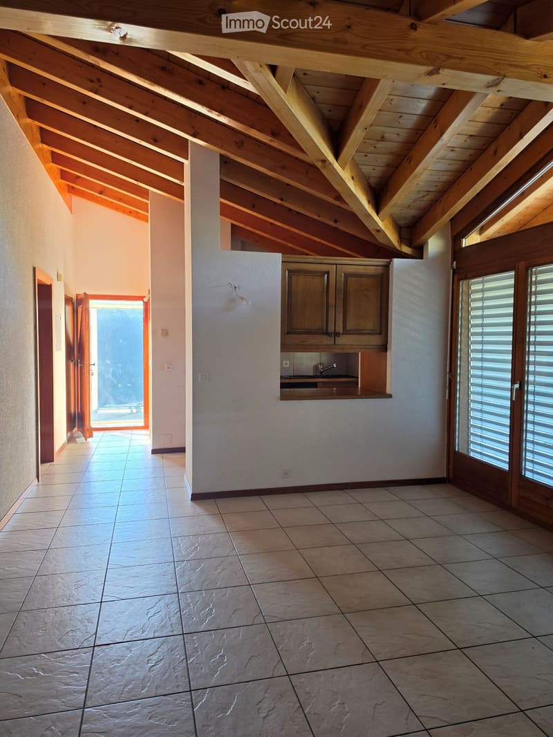 Empty room with exposed wooden beams on the ceiling, tiled floor, and a small built-in kitchen area with cabinets and a sink.