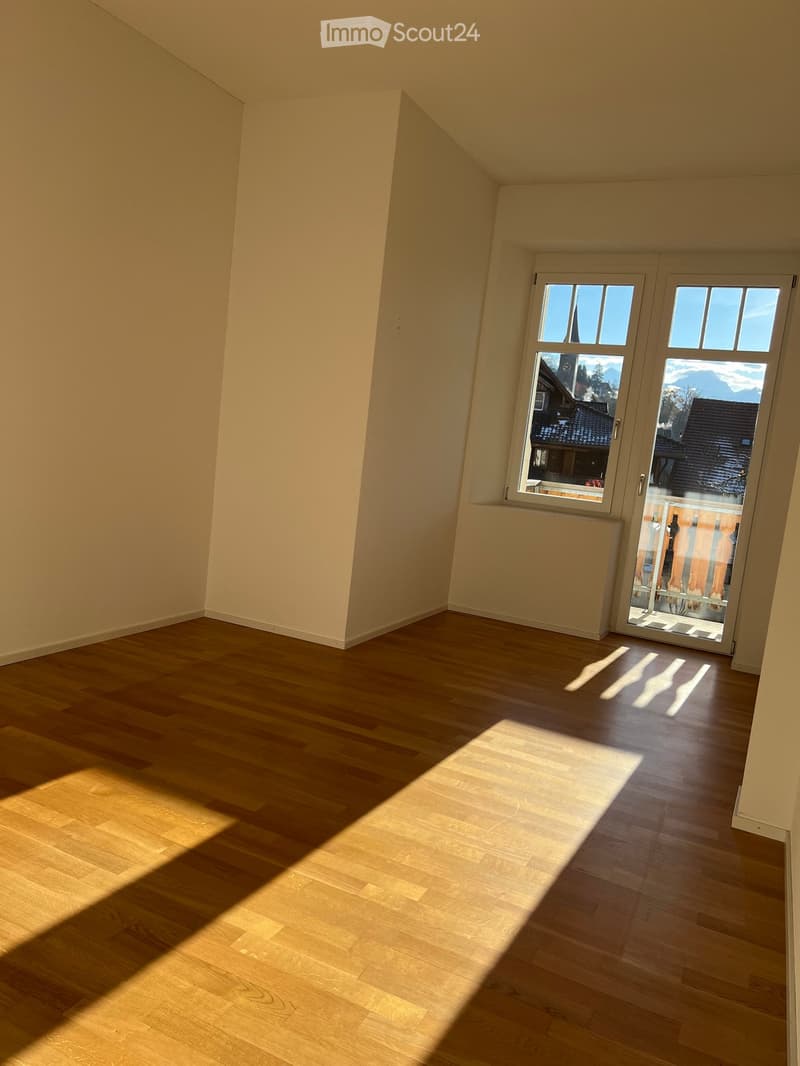 Empty room with wooden flooring and large windows, allowing natural light to fill the space.