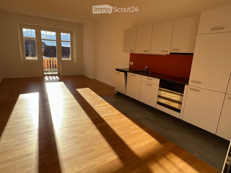 Modern kitchen with white cabinets, a dark countertop, and a red backsplash. The floor is wooden, and there is a window with a view of the mountains.