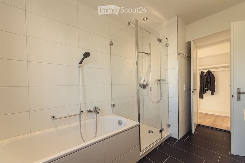 Modern bathroom with a bathtub, glass-enclosed shower, and a visible closet with hanging clothes.