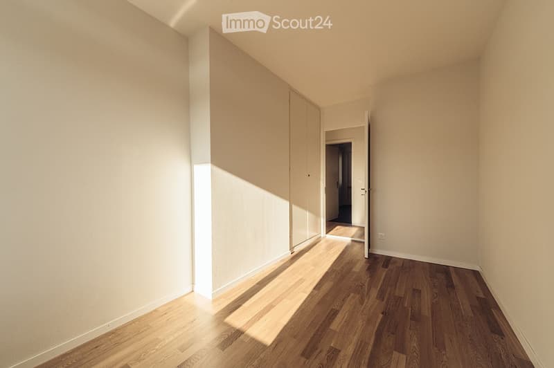 Empty room with light-colored walls and wooden flooring, featuring a closet and an open doorway leading to another space.