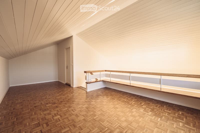 Completely empty room with wooden herringbone flooring, white walls, and a glass-railed balcony area.