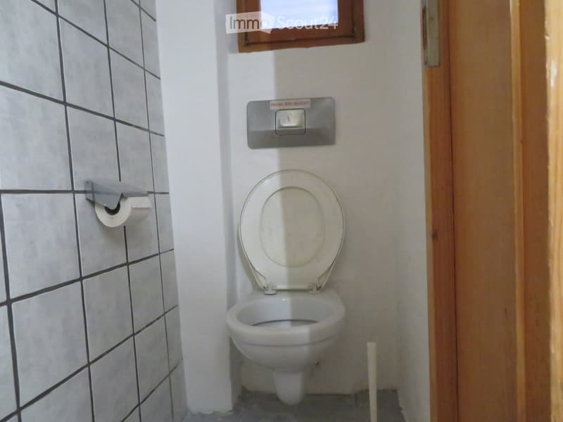 A small bathroom with a toilet, tiled walls, and a toilet paper holder mounted on the wall.