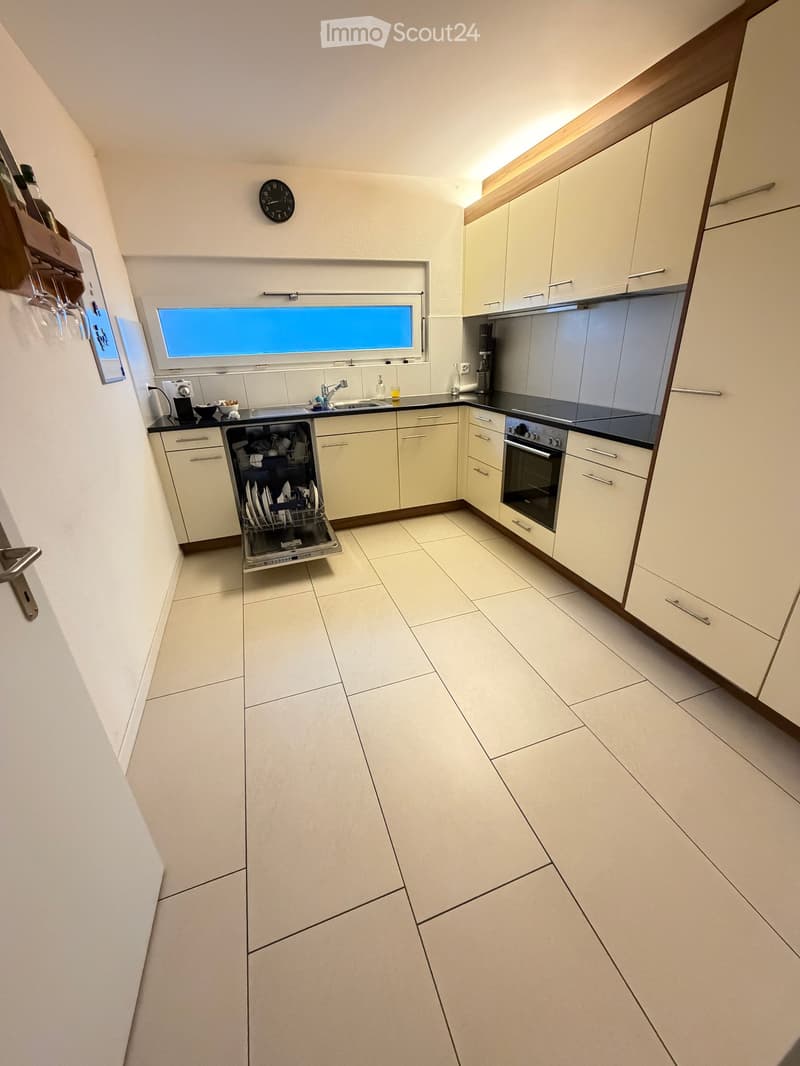 Modern kitchen with light-colored cabinets, a dishwasher, oven, sink, and a window above the sink.