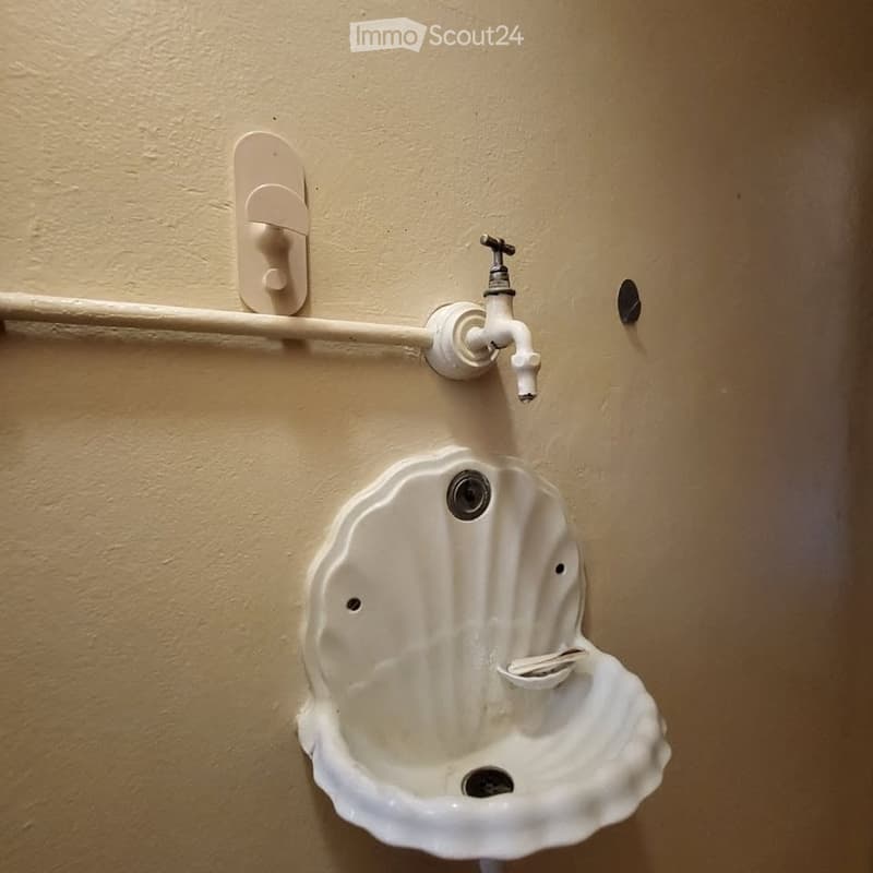 A small, shell-shaped sink with a faucet mounted on a beige wall.