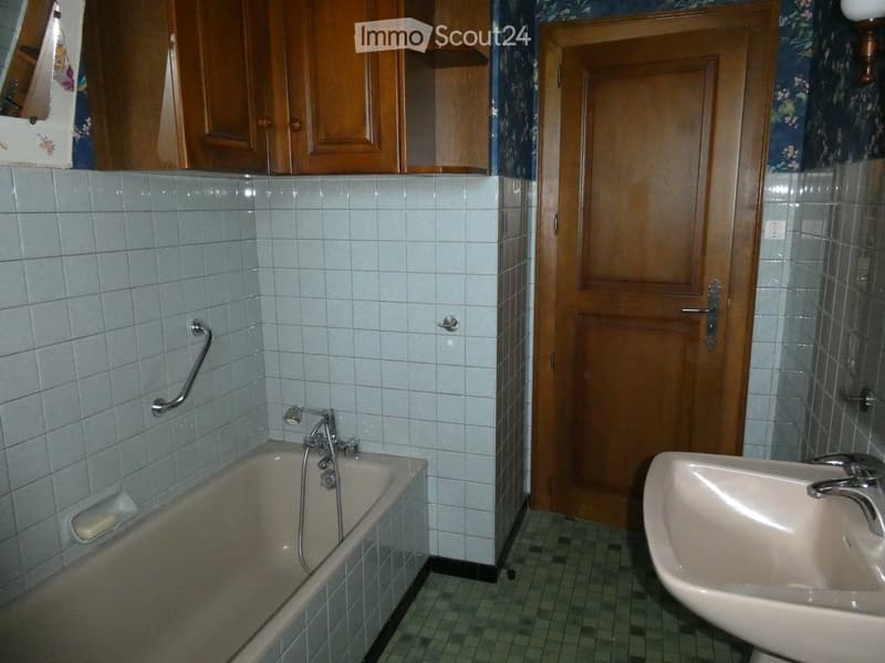 Bathroom with a bathtub, sink, faucet, handrail, and wooden cabinet.