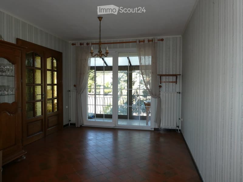 Empty hallway with wooden floor, large glass doors leading to a balcony, striped wallpaper, and a chandelier hanging from the ceiling.