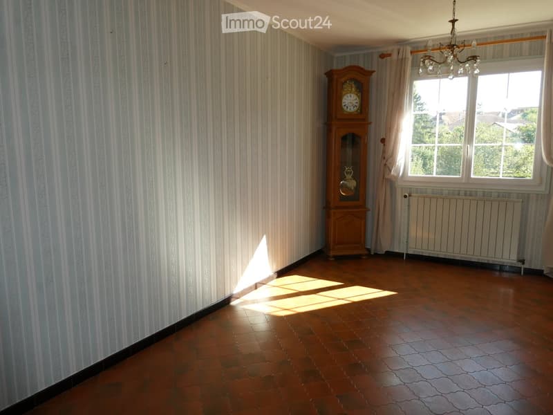 Empty room with striped wallpaper, wooden floor, large window with curtains, radiator, and a grandfather clock in the corner.