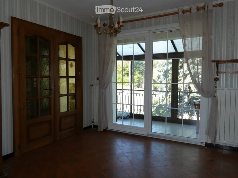 Empty room with wooden flooring, large sliding glass doors leading to a balcony, striped wallpaper, and a chandelier hanging from the ceiling.