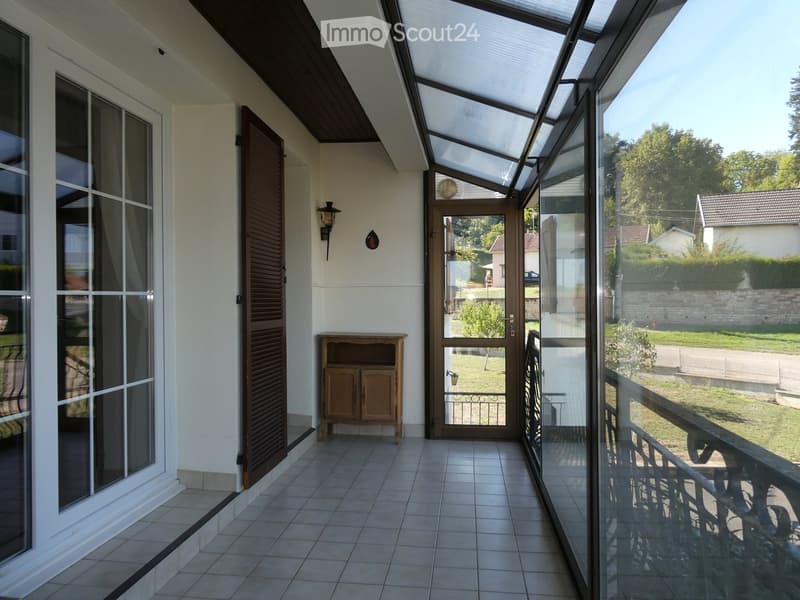 Balcony with tiled floor, glass enclosure, wooden cabinet, and view of the garden.