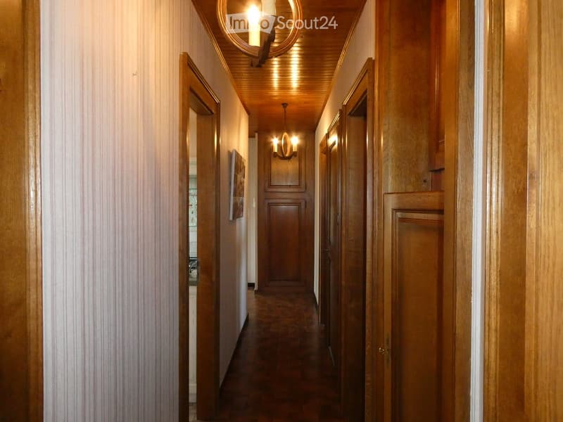 Wooden hallway with warm lighting, wooden doors, and a chandelier, leading to multiple rooms.