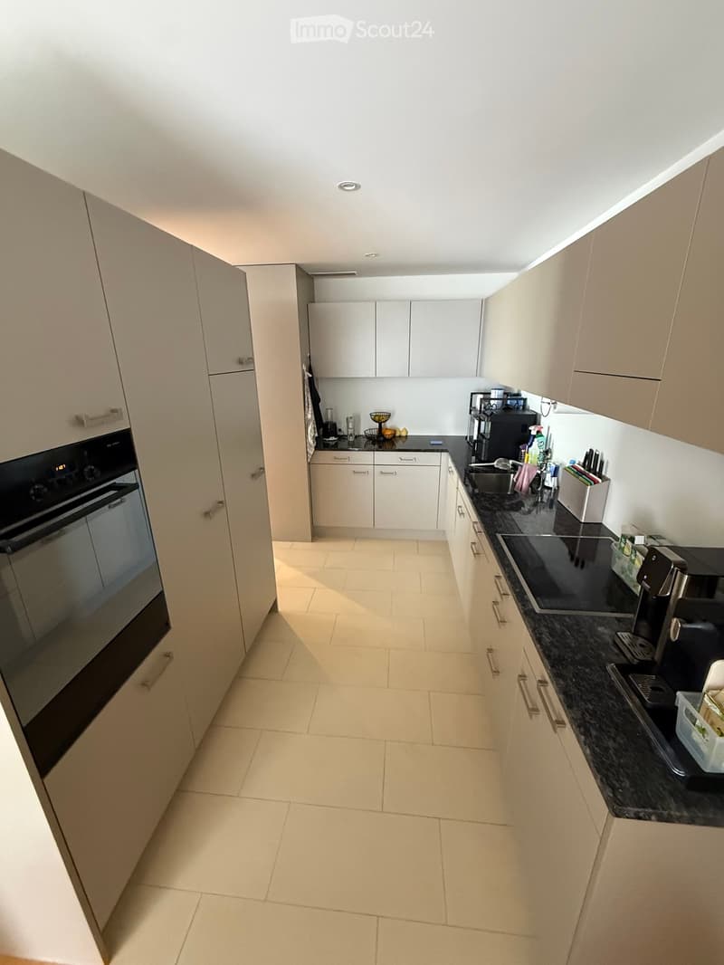Modern kitchen with light-colored cabinets, black countertops, and various appliances including an oven, coffee maker, and fridge.