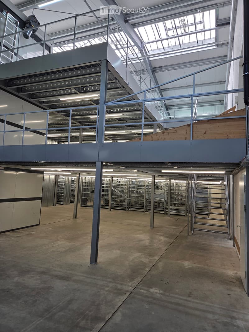 Empty industrial-style room with concrete floor, metal shelving units, and a raised platform with metal railings.