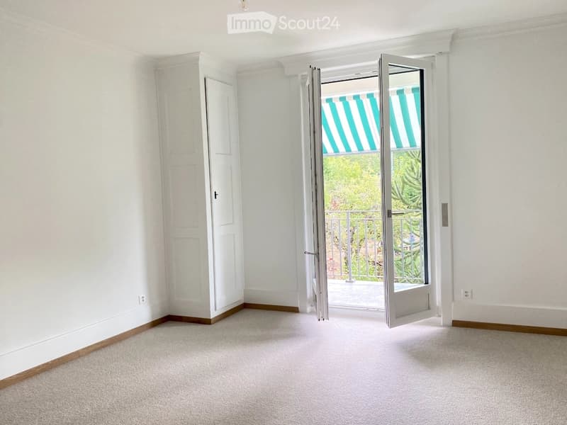 Empty room with white walls, carpeted floor, and a large sliding glass door leading to a balcony with striped blinds.