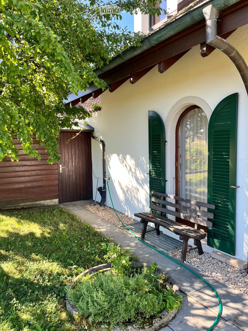 A small garden area with a wooden bench, green shutters, and a wooden garage door.