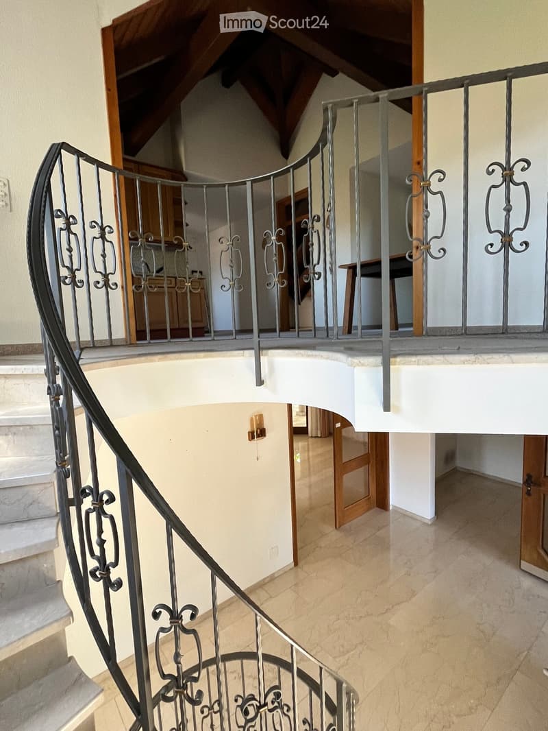 Spiral staircase with ornate metal railing, light-colored tiled floor, and visible doorways leading to other rooms.