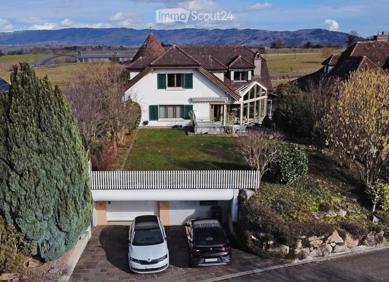 Two-story house with a garage, two parked cars, and a well-maintained garden with trees and a white picket fence.