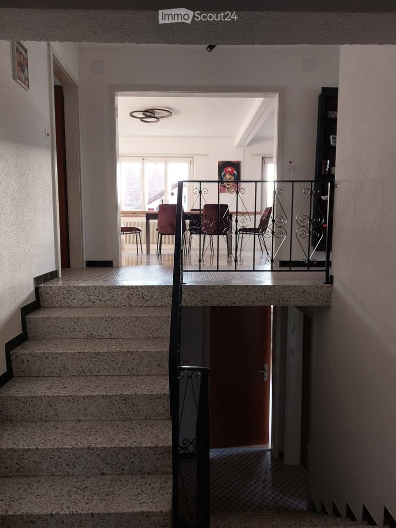 Staircase leading to an open area with a dining table and chairs, featuring a decorative metal railing and modern lighting.